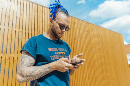 Young man with blue dreadlocks dancing reggaeton in the street. Man is on focus and foreground, wooden background is blurred.の写真素材