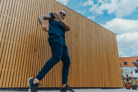 Young man with blue dreadlocks dancing reggaeton in the street. Man is on focus and foreground, wooden background is blurred.の写真素材