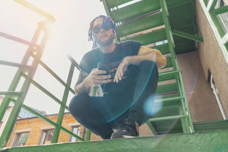 Young man with blue dreadlocks dancing reggaeton on green stairs. Man is on focus and foreground, green stairs is on background and blurred.の写真素材