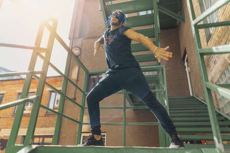 Young man with blue dreadlocks dancing reggaeton on green stairs. Man is on focus and foreground, green stairs is on background and blurred.の写真素材
