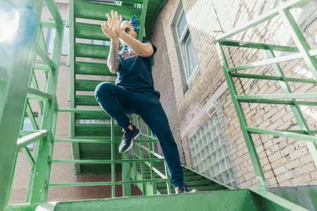 Young man with blue dreadlocks dancing reggaeton on green stairs. Man is on focus and foreground, green stairs is on background and blurred.の写真素材