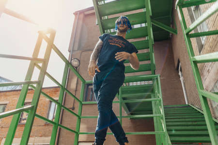 Young man with blue dreadlocks dancing reggaeton on green stairs. Man is on focus and foreground, green stairs is on background and blurred.の写真素材