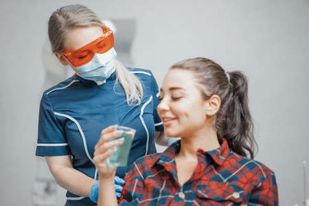 Close up of woman dentist giving plastic cup with water to a client .の写真素材