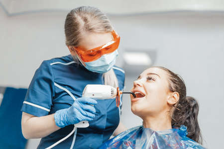 Close up of woman dentist holding curing lamp in client mouth.