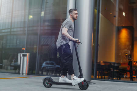 Attractive man riding a kick scooter at cityscape background.