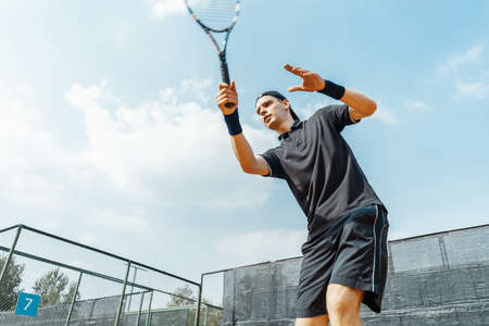 Young man playing tennis at tennis and serving a ball with straighten strike.