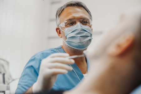 Close up of dentist in blue uniform checking up client teeth health condition.