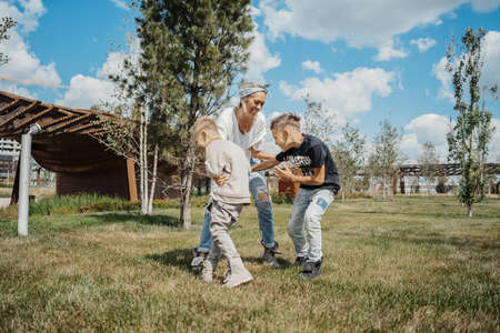 Young attractive mum having fun with her sons at green modern park.の写真素材