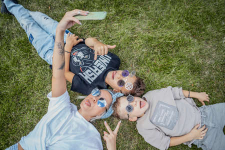 Close up of mum and sons lying in the park on green grass and making selfies. View from above. Happy family concept.の写真素材