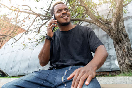 Close up of dark-skinned man in black T-shirt talking by mobile phone.