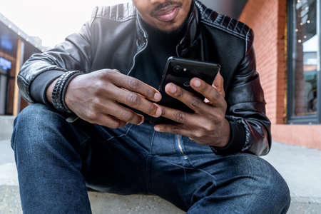 Close up of dark-skinned smiling man looking at mobile phone screen.