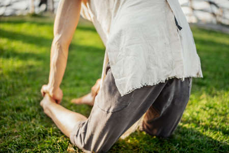 Close up of attractive athletic man practicing yoga and warming up in modern park at green grass outdoors.の写真素材