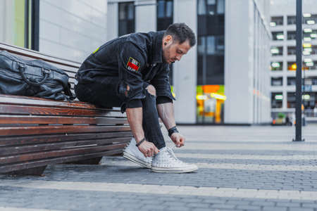 Attractive man tying laces of his sneakers and sitting on bench at downtown.の写真素材