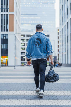 Attractive man passing through modern buildings and holding sports bag.の写真素材