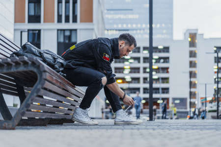 Attractive man tying laces of his sneakers and sitting on bench at downtown.の写真素材