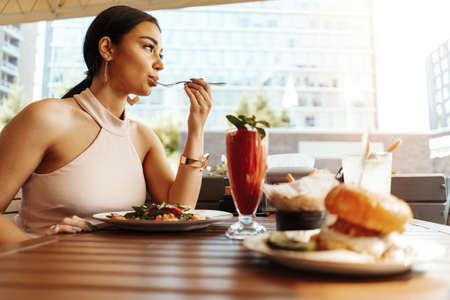 Close up of young attractive woman eating salad at street cafe.