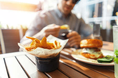 Close up of young attractive man eating french fries and burger at street cafe.の写真素材