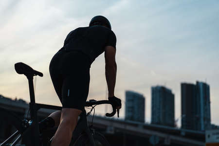 Silhouette of sportsman riding bike next to glass facades of skyscrapers.の写真素材
