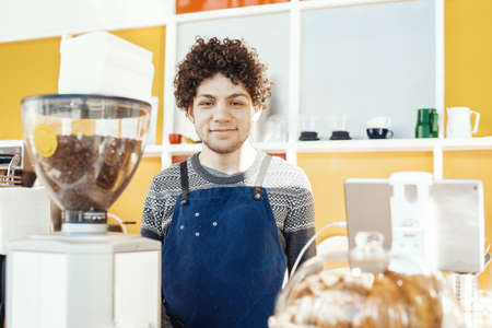 Friendly hospitable barista smiling and standing behind bar counter.の写真素材