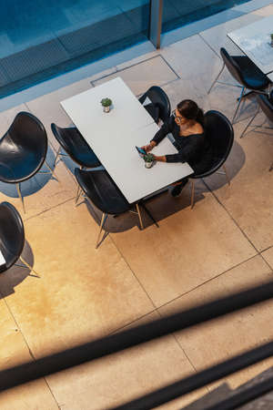 Young beautiful woman holding mobile phone in hands while waiting for her meal in modern cafe.の写真素材