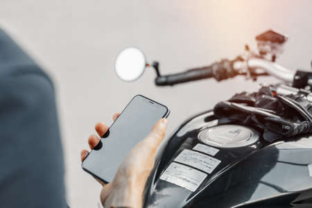 Close up of biker holding mobile phone while sitting on motorcycle.の写真素材