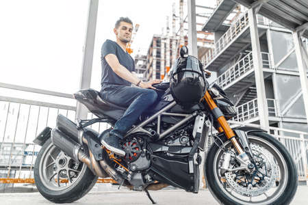 Handsome biker sitting on black motorcycle on urban background at parking.の写真素材