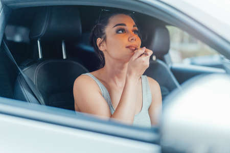 Close up of beautiful woman getting her lips painted while sitting in car.の写真素材