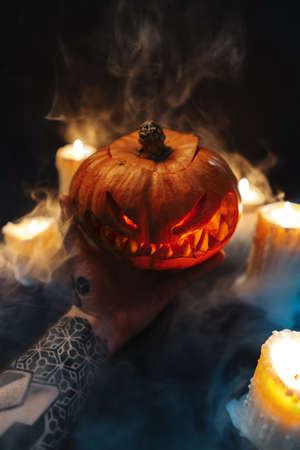 Man hand holding carved Halloween pumpkin on dark background.