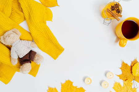 Autumn composition flat lay. Cup of tea, women fashion sweater, bear toy, dried leaves, honey jar, candles, cinnamon sticks and anise on light background. Comfortable and cozy autumn, fall concept.の写真素材