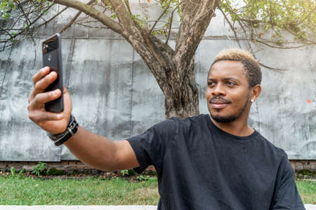 Close up of dark-skinned man in black T-shirt making selfie on mobile phone.