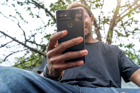 Pensive dark-skinned man in black T-shirt looking at mobile phone screen.
