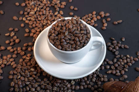 Close up of coffee cup and croissant in coffee beans on black background.の写真素材