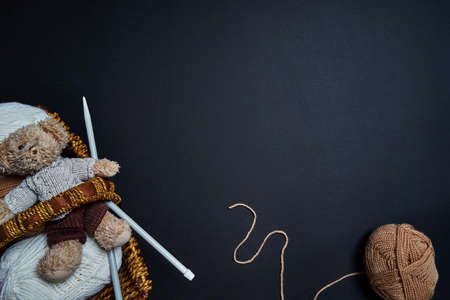 Knitting yarn, bear toy and knitting needles in basket on dark background.
