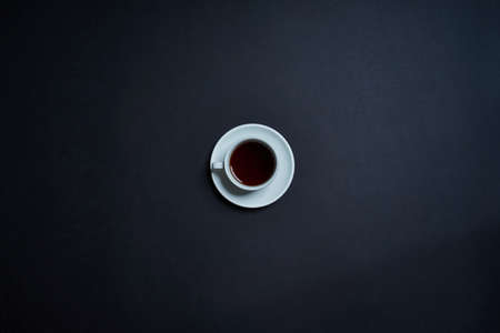 Flat lay of white cup with tea on dark background.