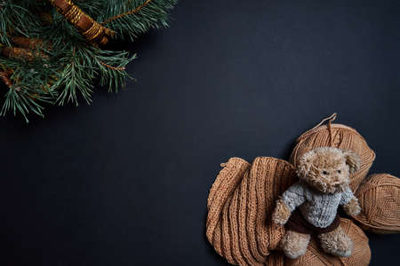 Flat lay of knitting yarn, bear toy and basket with pine branches on dark background.の写真素材