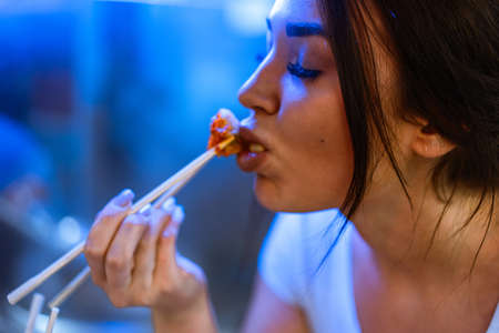 Close up of young attractive woman eating asian food with chopsticks at cafe.の写真素材