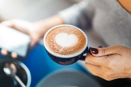 Close up of woman hands holding cup of coffee and mobile phone.