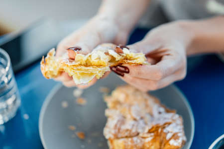 Close up of woman hands breaking in pieces fresh croissant with almond.の写真素材