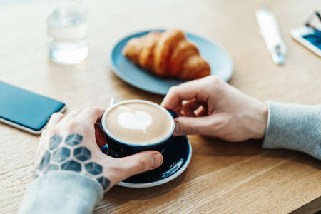 Man hands holding cup of coffee. Croissant and mobile phone are on background.の写真素材
