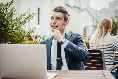 Young pensive businessman sitting next to laptop and touching his chick.