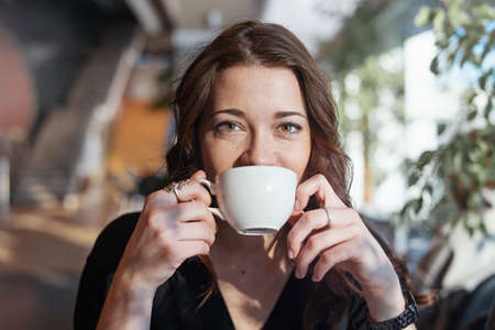 Attractive woman drinking tea at lunch break from white cup and smiling.
