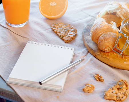 Close up of Blank notepad near Croissant and oat cookie, honey jar and orange juice on wooden table with rustic linen tablecloth. Healthy breakfast and making plans for a day Concept.の写真素材