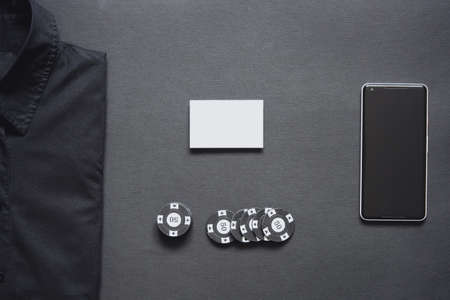 Casino chips, formal shirt, blank business card and mobile phone on minimalistic black background. Casino game. Online casino. Gambling concept, poker mobile app. Poker game theme.の写真素材