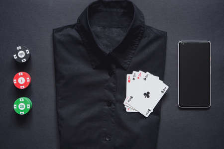 Casino chips, playing cards on formal black shirt and mobile phone on minimalistic black background. Casino game. Online casino. Gambling concept, poker mobile app. Poker game theme. set of four acesの写真素材