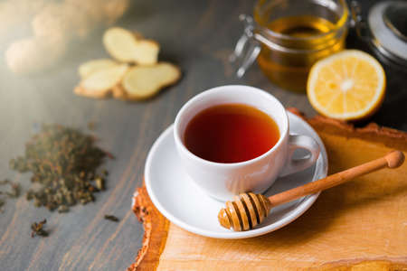 Close up of Cup of tea with lemon, ginger, honey and honey stick on wooden rustic table. Concept of natural cough remedy , healing and treatment. Beverage rich of vitamins for autumn and winter.の写真素材