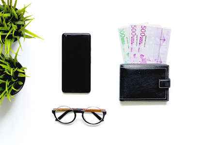 Flatlay of money in black wallet, mobile phone, glasses on white background. Top view. business...