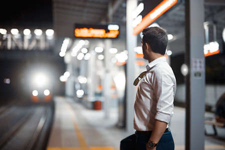 Young attractive businessman waiting for train in metro or subway on modern stylish platform. Concept of commuting.の写真素材