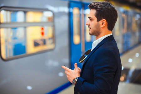 Young attractive businessman texting message in mobile phone while waiting for train in metro....