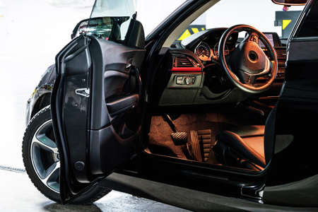 Dark luxury car Interior . steering wheel, shift lever and dashboard. Car interior luxury. clima te control, speedometer, display, Black panels. View from open door outside the car.の写真素材