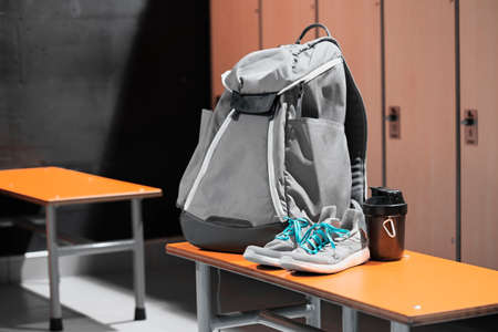 Close up of sports shoes, sport backpack and sport water bottle in gym locker room. Concept of active lifestyle, gaining muscles or loosing fat. Sport equipment.